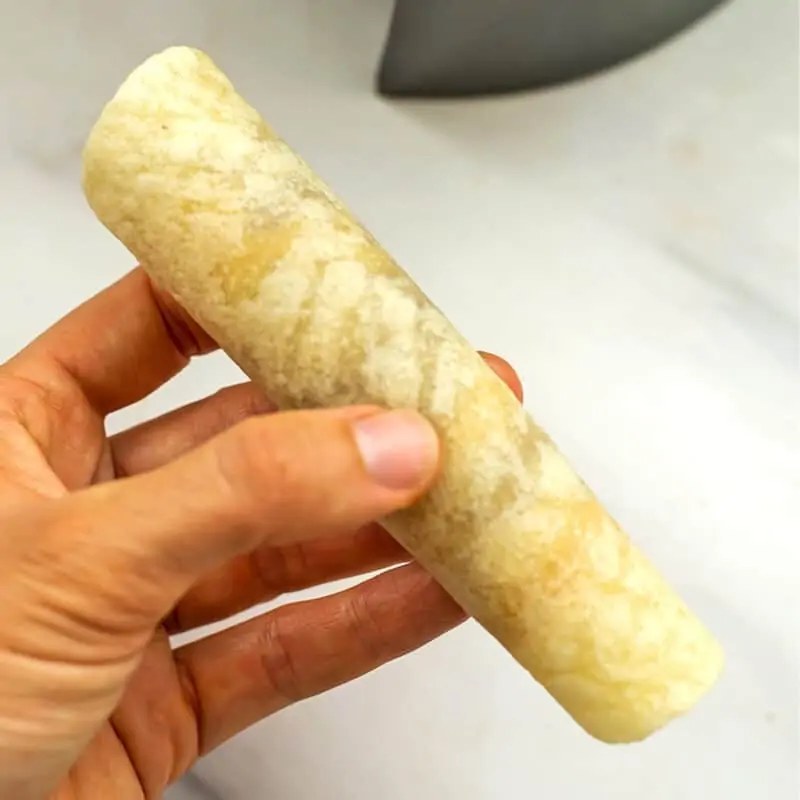Hand holding a vegan taquito before putting in air fryer.