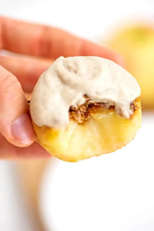 Hand holding baked apple with frosting with a large bite removed.