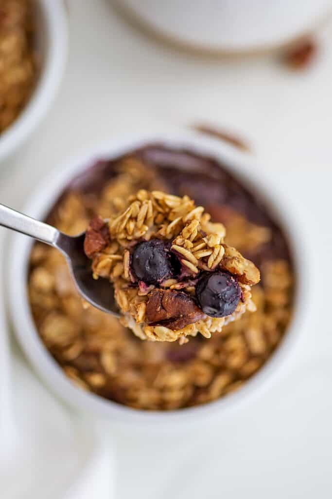 Spoon holding blueberry pecan baked oats over single ramekin.