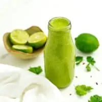 Bottle of cilantro lime dressing with limes and cilantro around bottle.