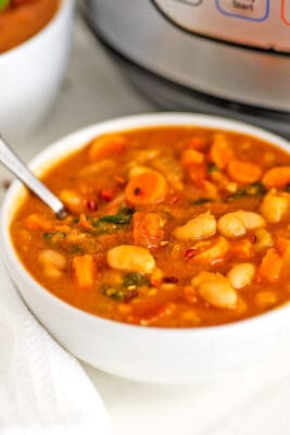White bowl filled with instant pot white bean soup with spoon.
