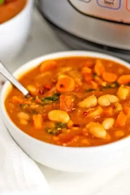 White bowl filled with instant pot white bean soup with spoon.