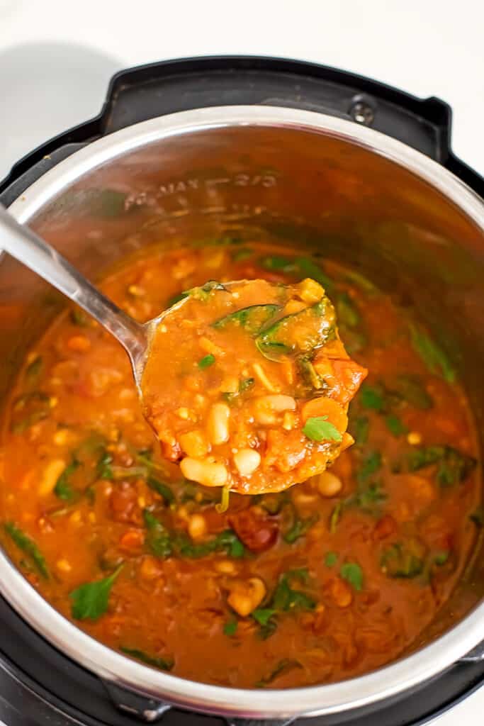Silver ladel spooning out a serving of tuscan white bean soup.