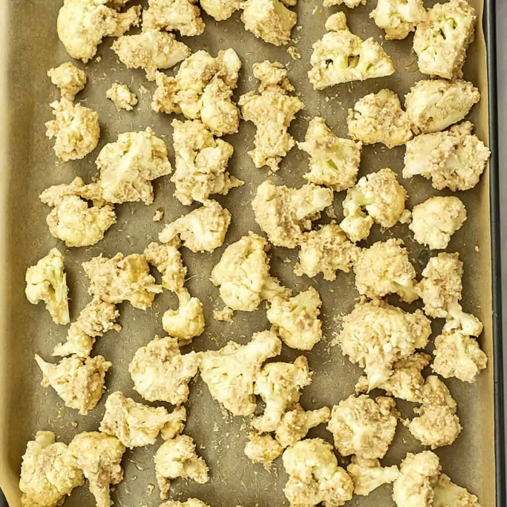 Coated cauliflower florets on a baking sheet lined with parchment.