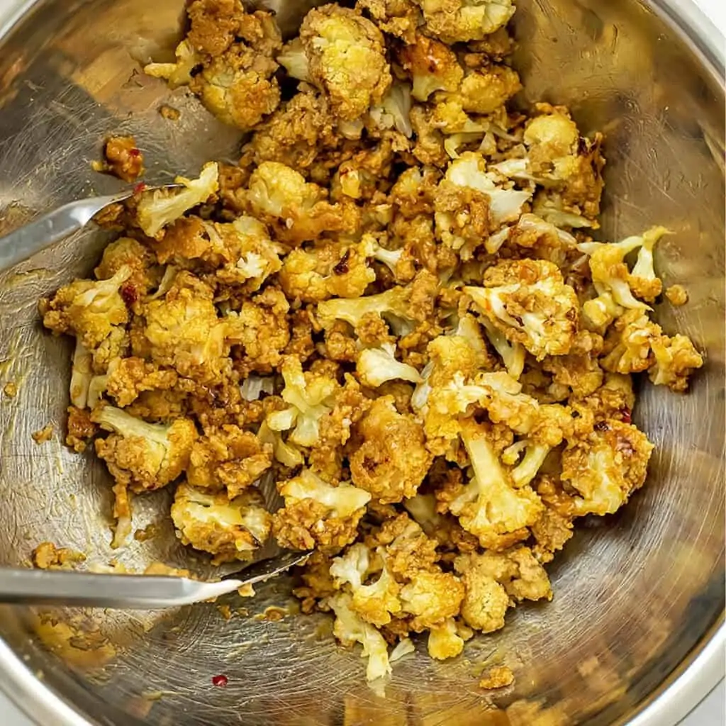 Crispy cauliflower after being tossed with orange sauce in large silver bowl.