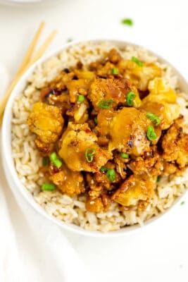 Orange cauliflower over rice in a white bowl.
