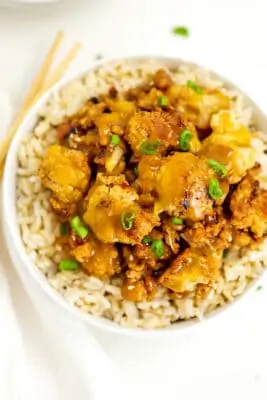 Orange cauliflower over rice in a white bowl.
