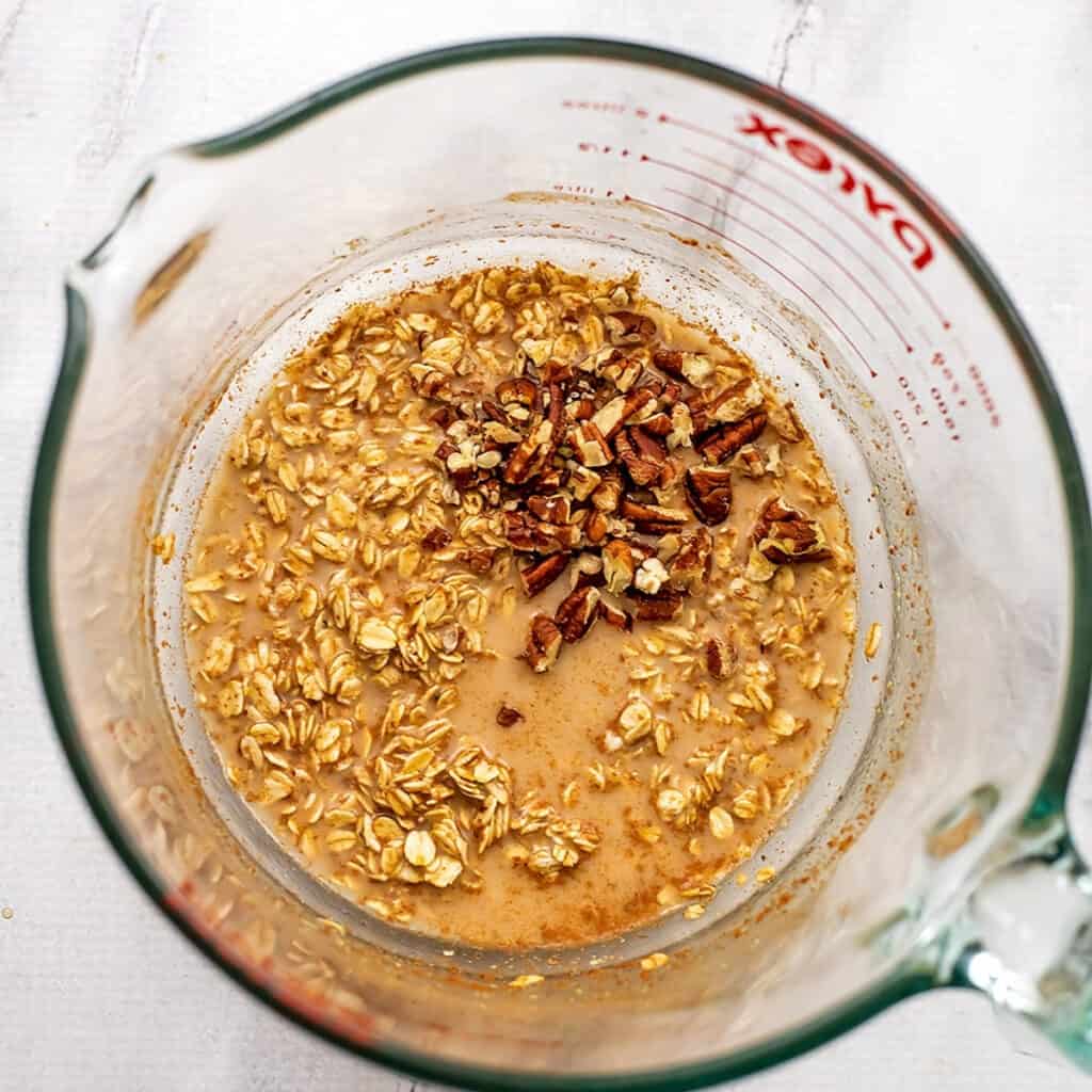 Glass jar with liquid, oats and pecans adds.