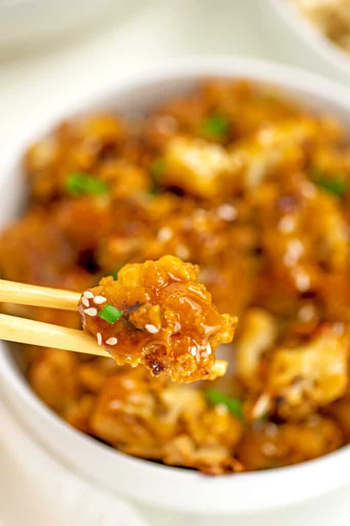 Vegan orange chicken in a bowl with chopsticks picking up a piece.