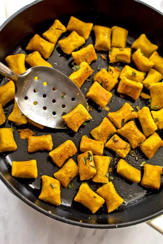 Spoon turning over gluten free pumpkin gnocchi in a skillet.