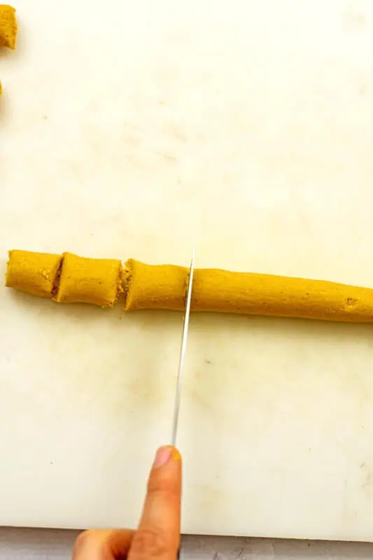 Knife cutting the log of pumpkin gnocchi dough into small gnocchi pieces.