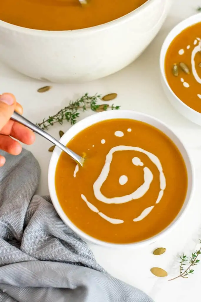 Hand holding spoon in bowl of butternut squash soup.