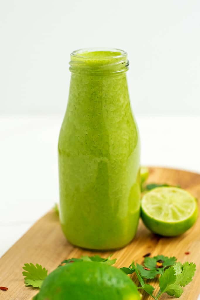 Bottle of cilantro lime vinagrette on wooden cutting board. 