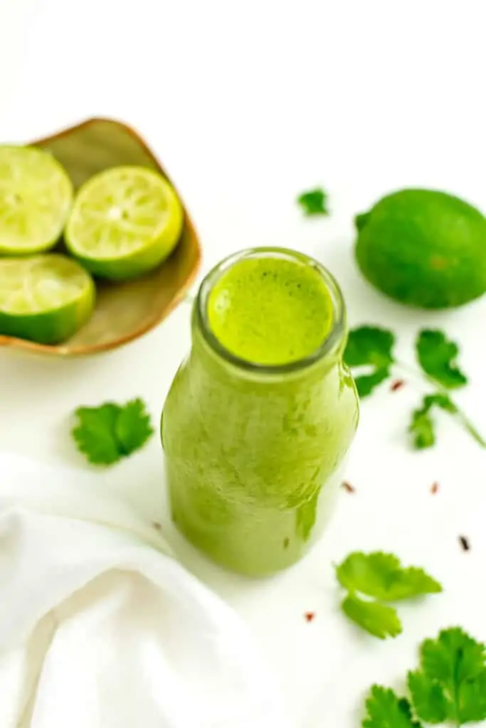 Cilantro lime dressing in a glass bottle with squeezed limes in bowl.