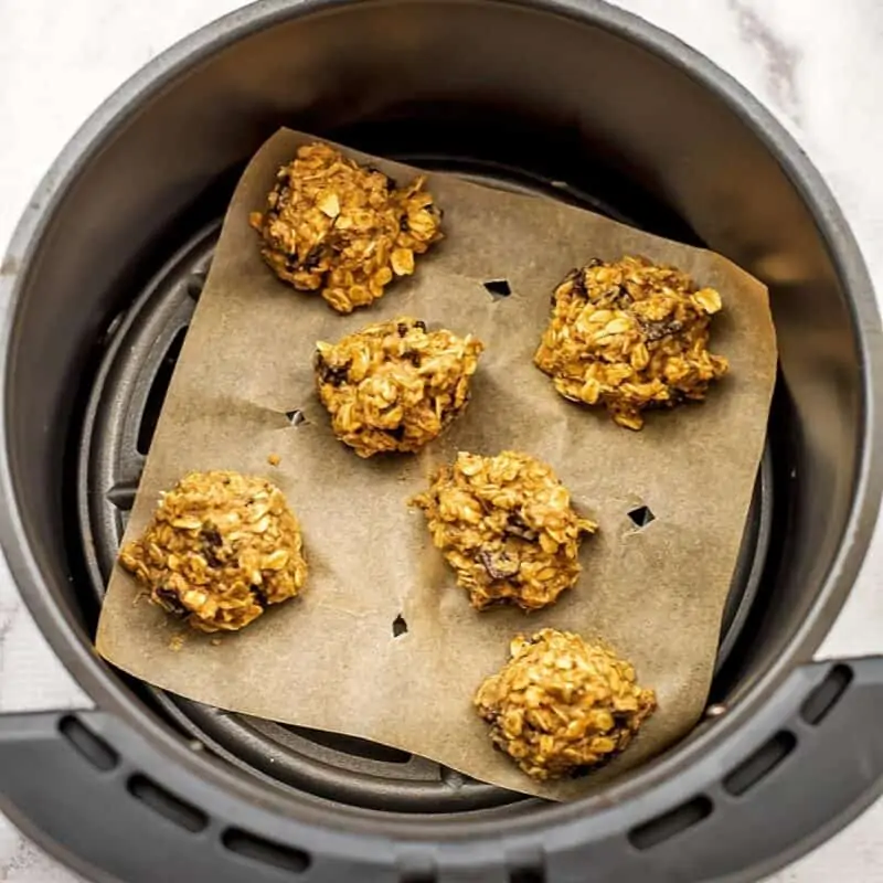Vegan oatmeal cookie batter scooped in balls on parchment in air fryer.