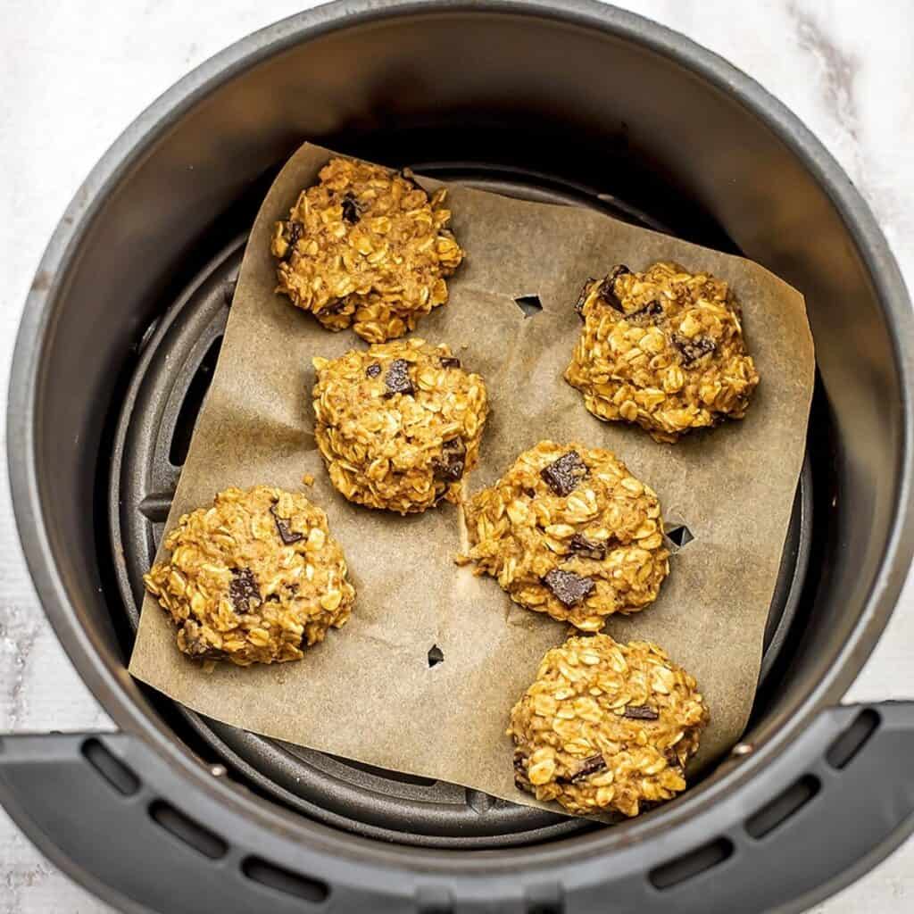 Oatmeal cookies pressed down on parchment paper in air fryer.