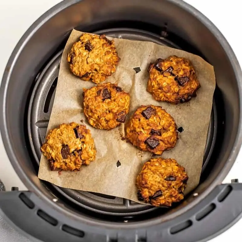 Chocolate chip oatmeal cookies on parchment paper in air fryer.