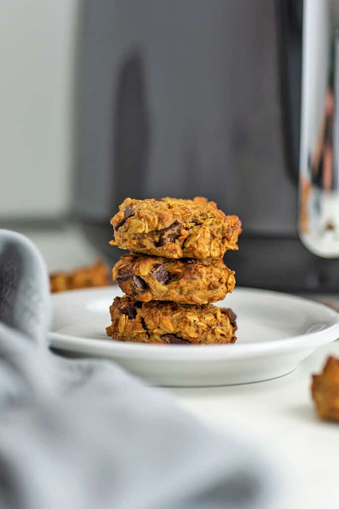 Chocolate chip oatmeal cookies stacked on a plate in front of air fryer. 