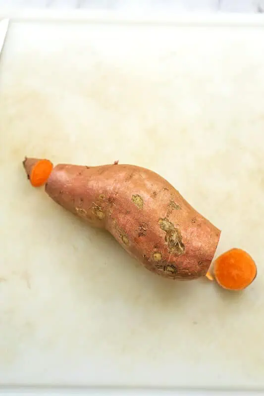 sweet potato with top and bottom cut off on white cutting board