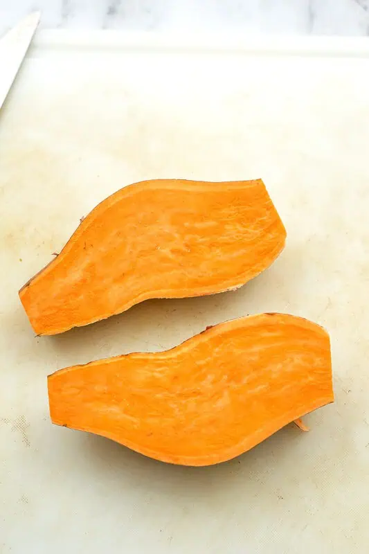 sweet potato cut in half lengthwise on white cutting board.
