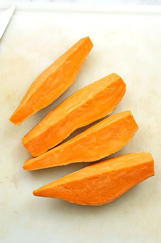 sweet potato cut into quarters on white cutting board.