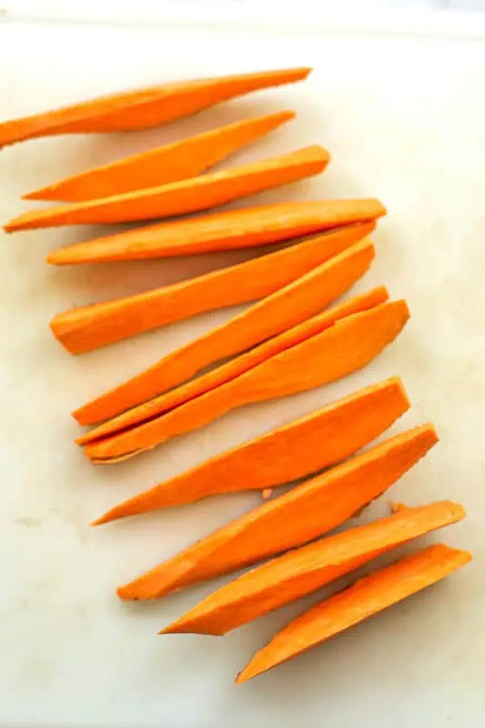 Sweet potato cut into 12 wedges on white cutting board.