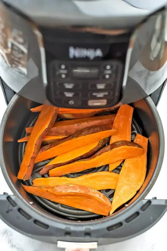 Sweet potato wedges in a single layer in the air fryer basket before cooking.