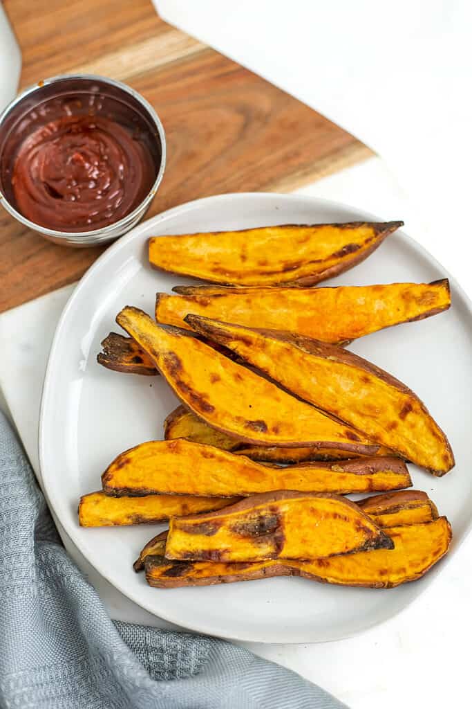 White plate with air fry sweet potato wedges and ketchup.