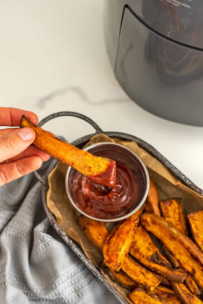 Sweet potato wedge being dunked in ketchup.