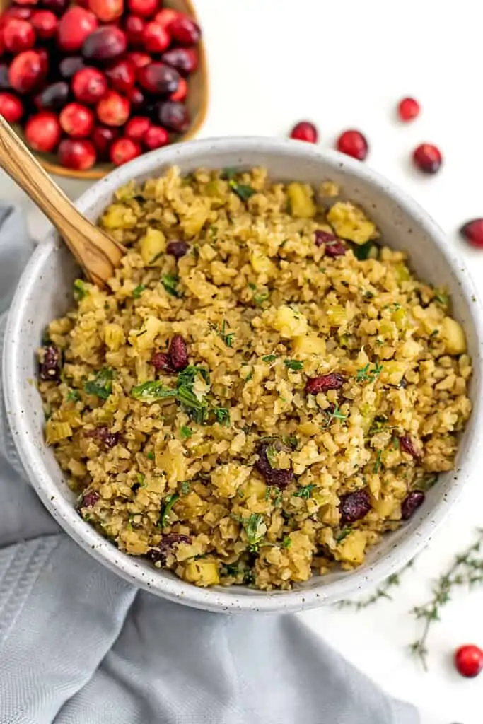 Bowl filled with cauliflower stuffing with cranberries in background.