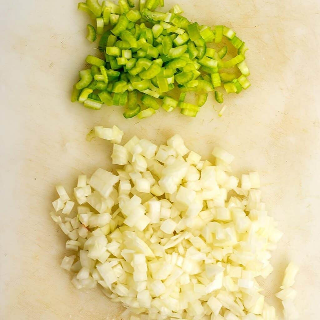 Chopped celery and chopped onion on white cutting board.