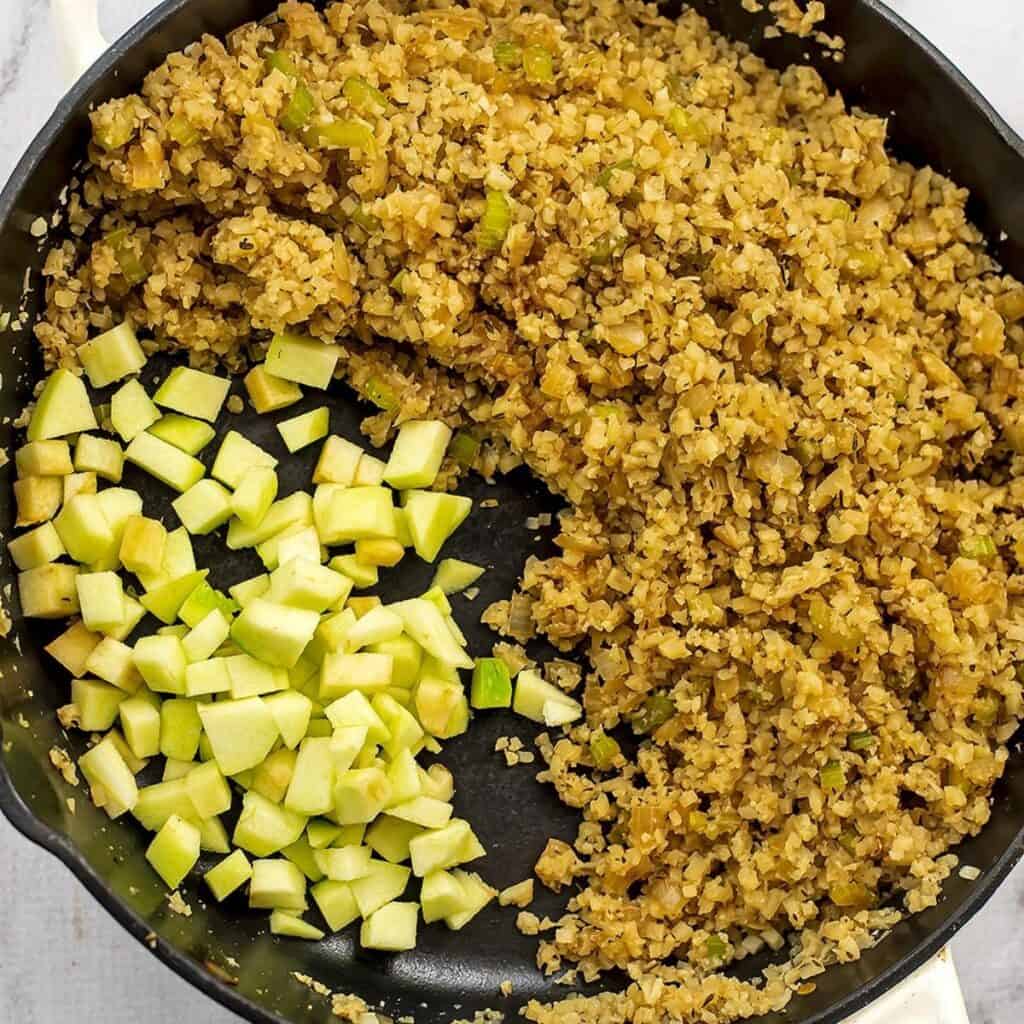 Diced apples being added to cauliflower mixture in skillet.