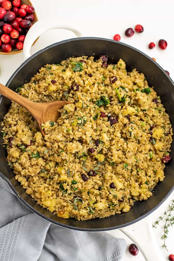 Skillet filled with cauliflower rice stuffing with wooden spoon. 
