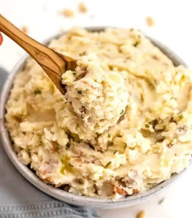 Spoon with Whole30 mashed potatoes on the spoon over a bowl of potatoes.