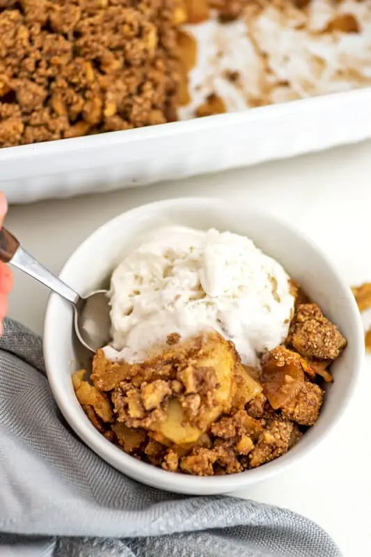 Scoop of ice cream in a bowl with apple crumble in the bowl.