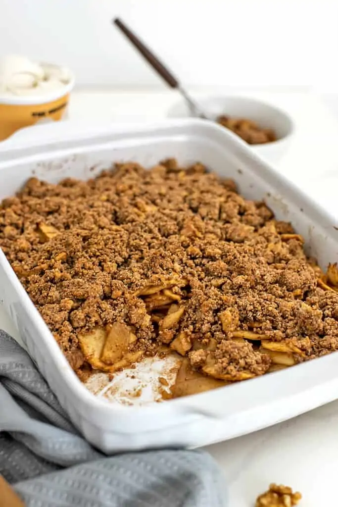 Apple crumble in the white casserole dish with ice cream in background.