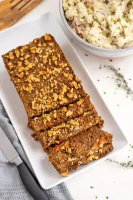 Lentil walnut loaf sliced into 3 pieces on a white platter.