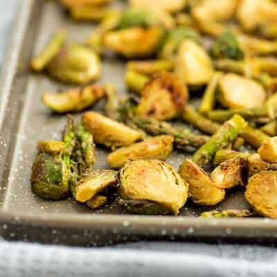 Roasted asparagus and brussel sprouts on baking sheet.