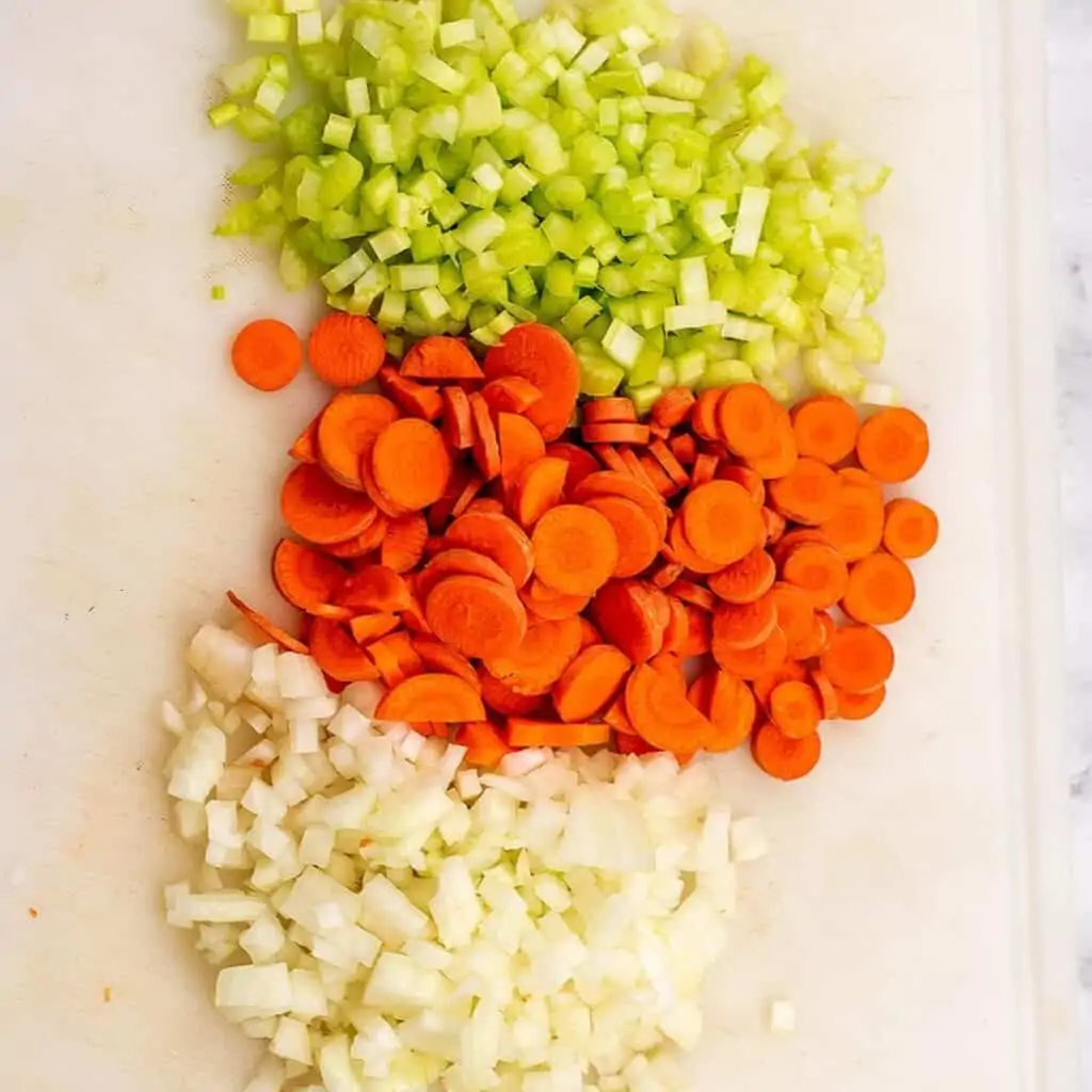 Chopped celery, carrots and onion on white cutting board.