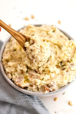 Spoon with Whole30 mashed potatoes on the spoon over a bowl of potatoes.