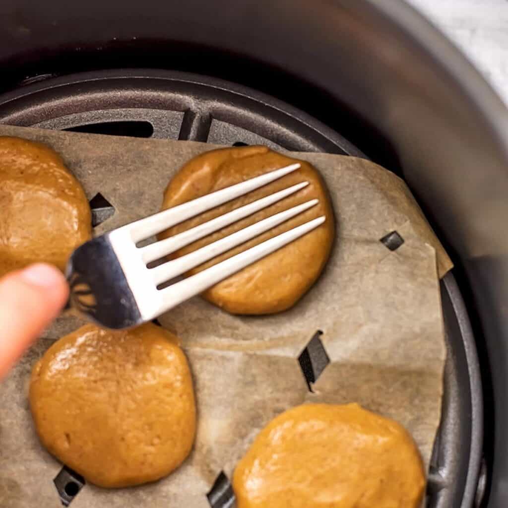 Fork pressing down on peanut butter cookies in air fryer.