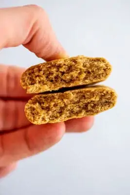 Peanut butter cookie cut in half being held in one hand.