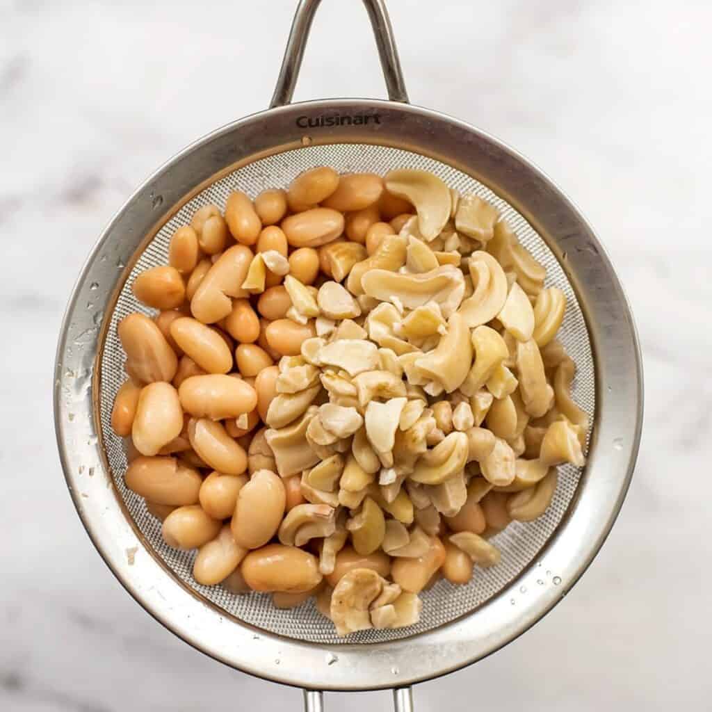 White beans and raw cashews in mesh strainer.