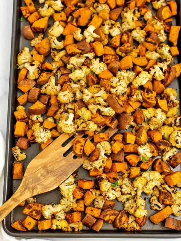 Sheet pan filled with roasted cauliflower and sweet potatoes with wooden spatula.