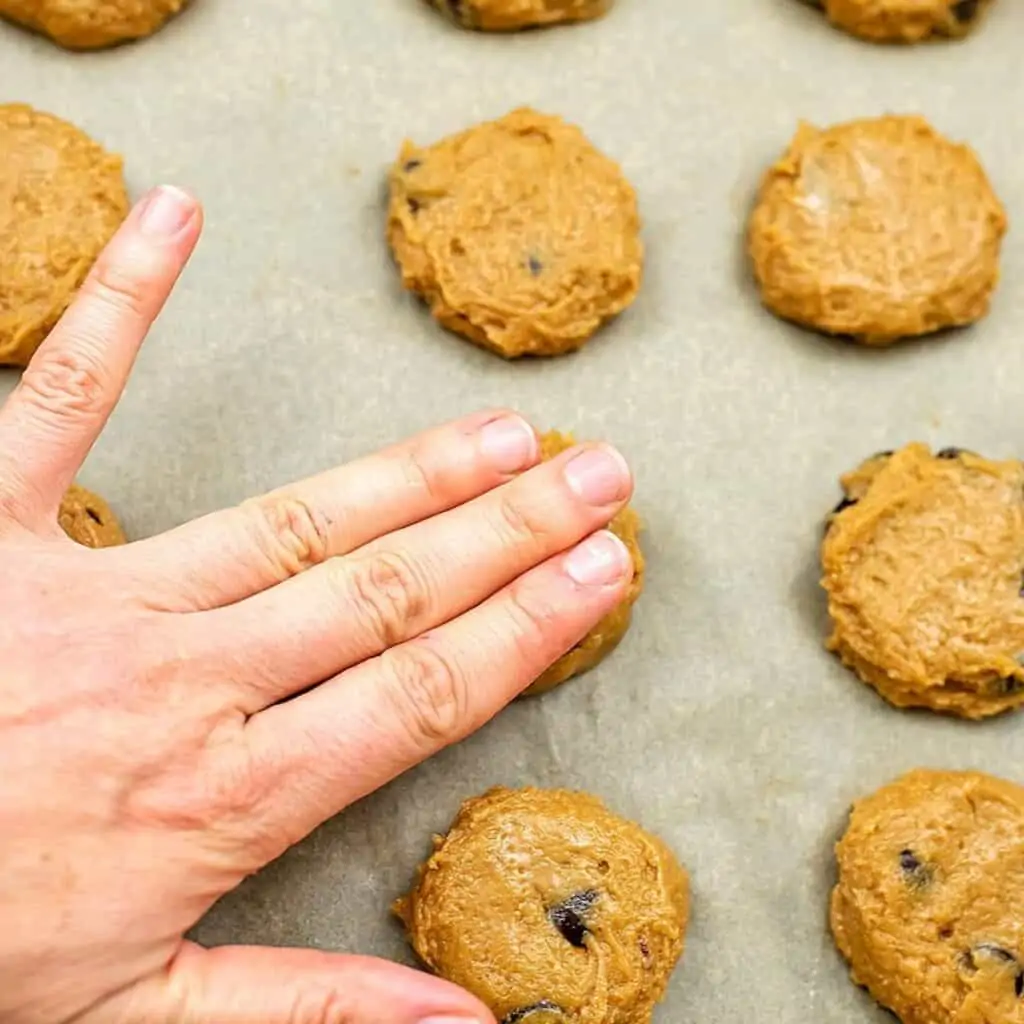 Hand flattening cookies on baking sheet.