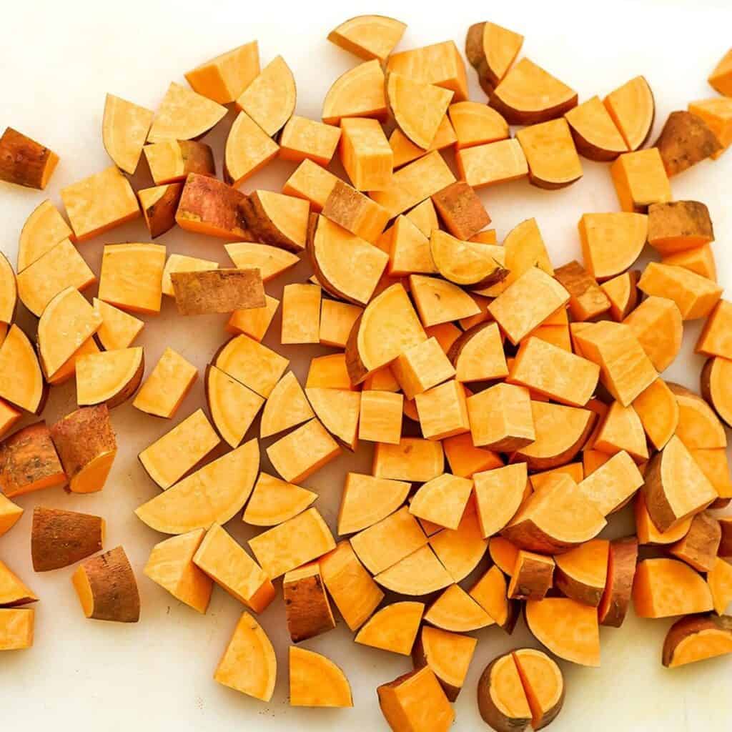 Chopped sweet potatoes on white cutting board.