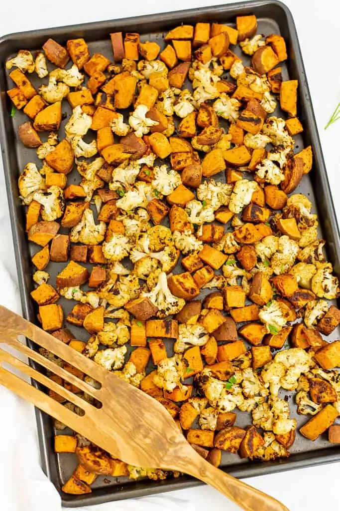 Roasted cauliflower and sweet potatoes on sheet pan with wooden spatula. 