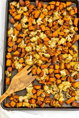 Sheet pan filled with roasted cauliflower and sweet potatoes with wooden spatula.