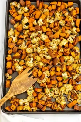 Sheet pan filled with roasted cauliflower and sweet potatoes with wooden spatula.