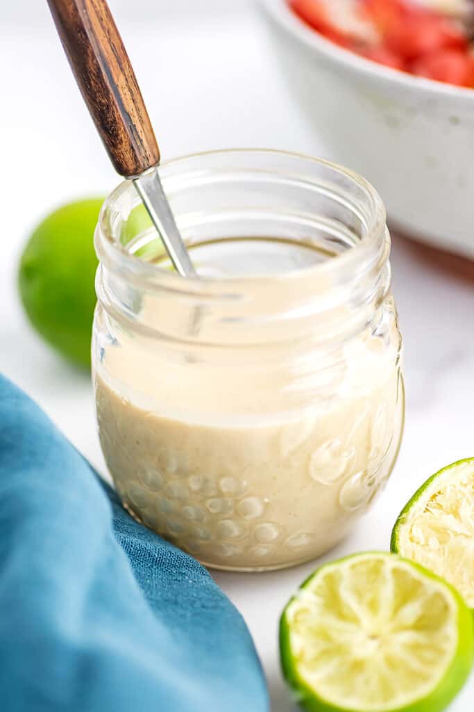 Wooden spoon in jar filled with lime tahini dressing.